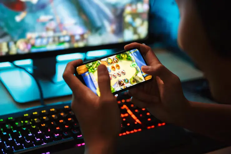 Cross-Platform Game Development Teenage gamer playing video games on a smartphone in a dark room.