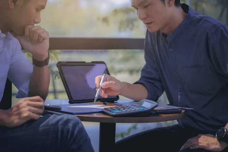 Console game development agency in Canada working on monetization strategies with two people, a calculator, and a tablet on the table